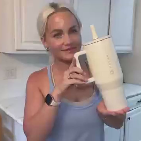 Woman holding HydroJug Tumbler – 32OZ Stainless Steel Vacuum Insulated Travel Mug with Straw Lid in kitchen.