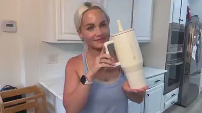 Woman holding HydroJug Tumbler – 32OZ Stainless Steel Vacuum Insulated Travel Mug with Straw Lid in kitchen.